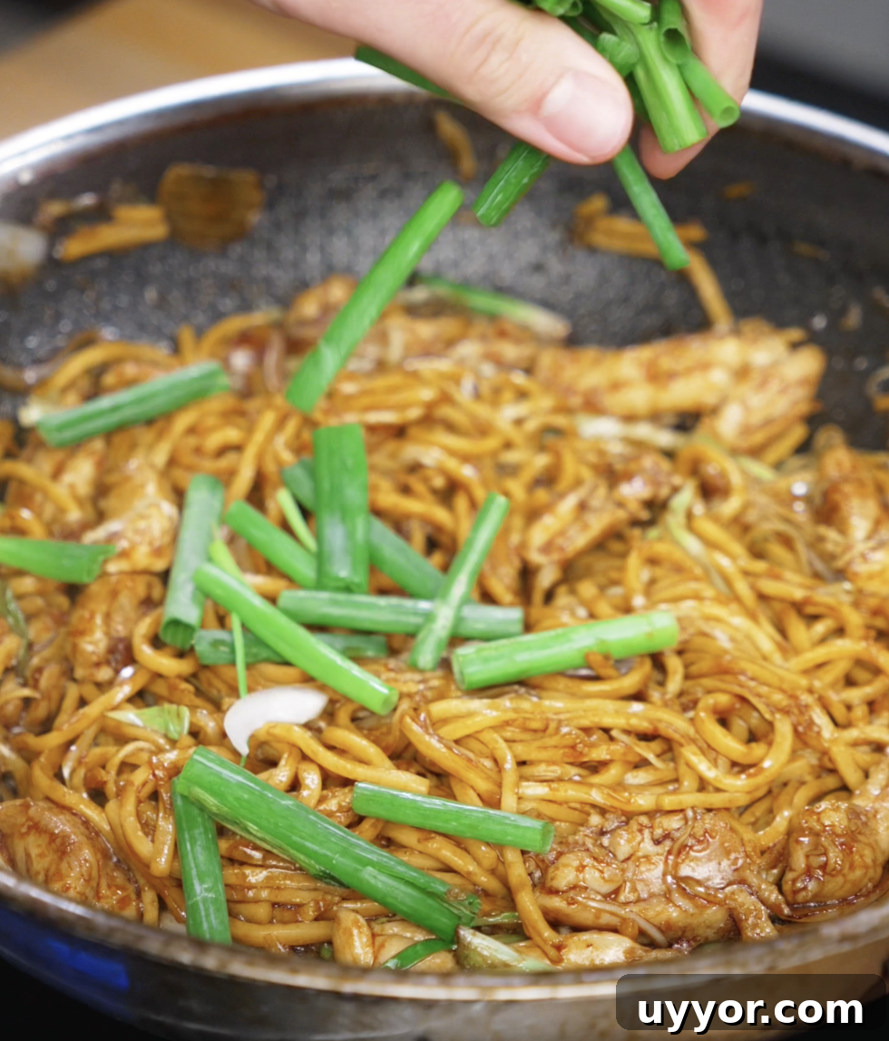 Crispy Pan-Fried Chicken Noodles with Soy-Garlic Sauce 10 Fresh scallion greens are being added to the pan as the final touch. They add a pop of color, crunch, and brightness to the finished noodles.