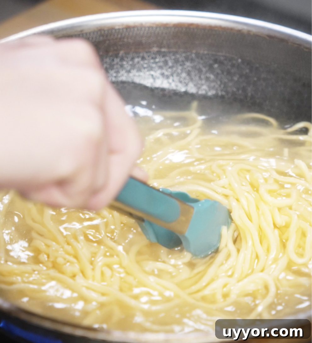 Crispy Pan-Fried Chicken Noodles with Soy-Garlic Sauce 5 Fresh wheat noodles are boiling in a pot of water, stirred with tongs to prevent sticking. These chewy noodles form the base of the pan-fried dish.