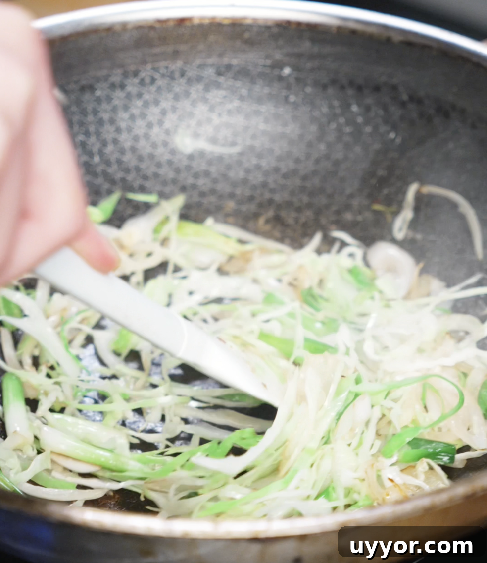 Crispy Pan-Fried Chicken Noodles with Soy-Garlic Sauce 8 Sliced onions and scallion whites are being sautéed in a wok. These vegetables create an aromatic base for the sauce to cling to later.