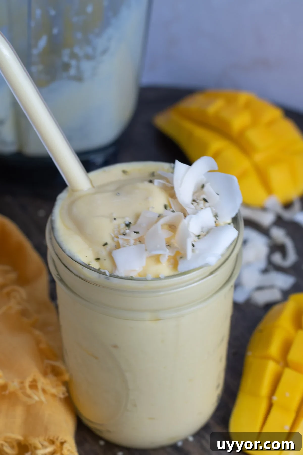 Mason jar with pale orange mango protein smoothie in it- topped with coconut flakes and hemp hearts