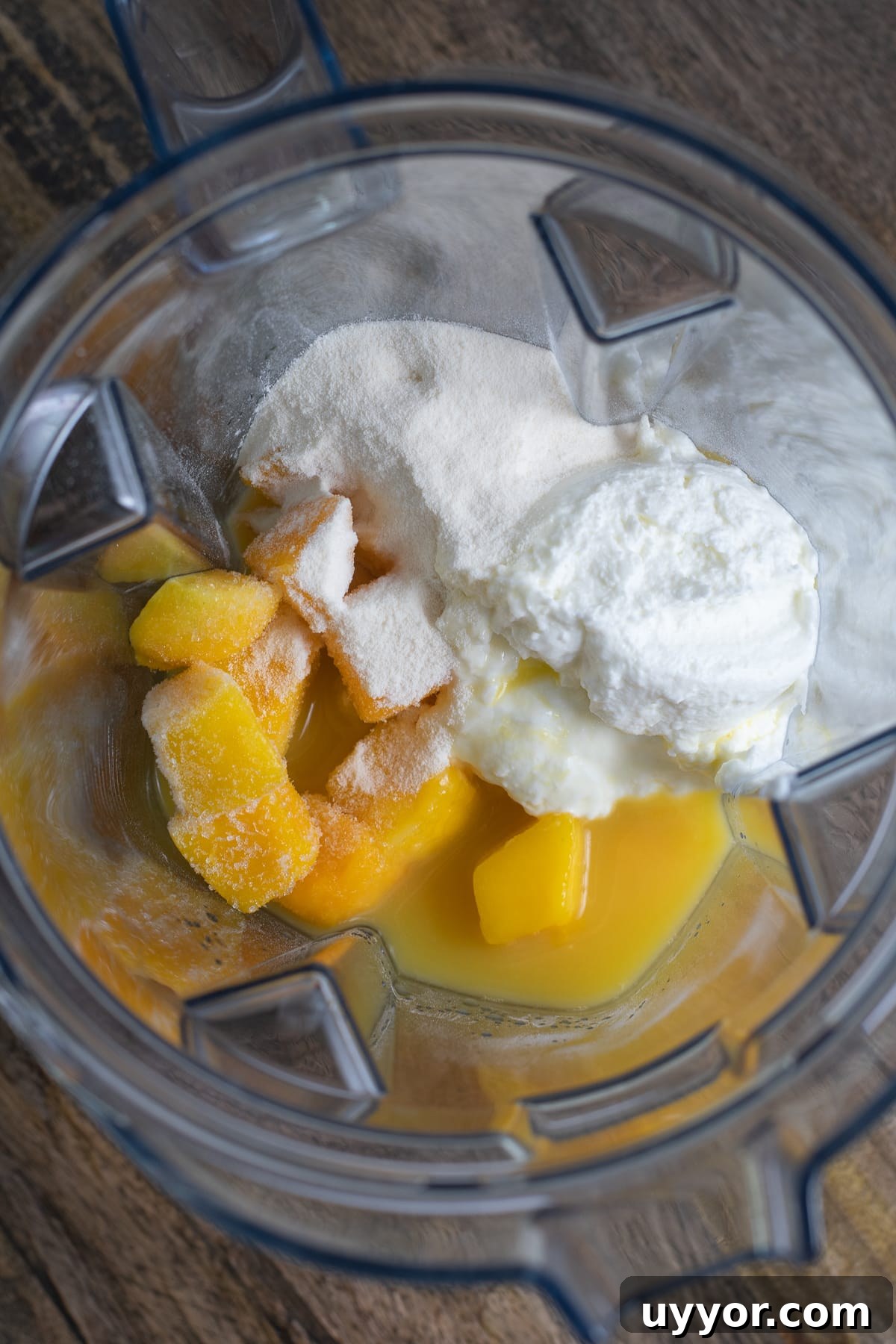 Overhead view of blender pitcher with protein powder, frozen mango, orange juice and Greek yogurt in it