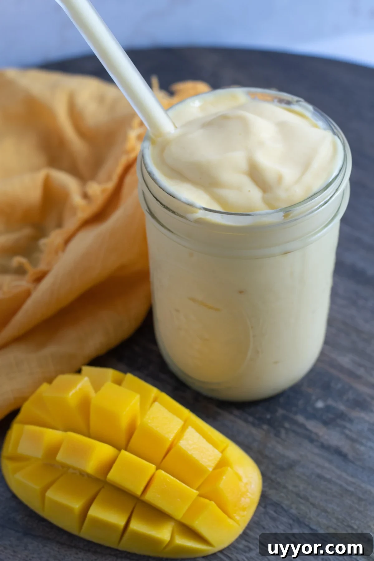 mango smoothie in mason jar with an orange napkin and half a chopped mango