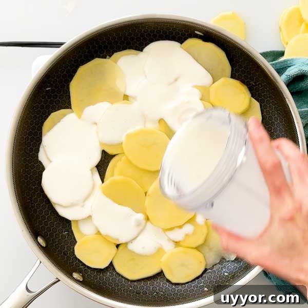 Pouring cream over the first layer of sliced potatoes in the skillet.