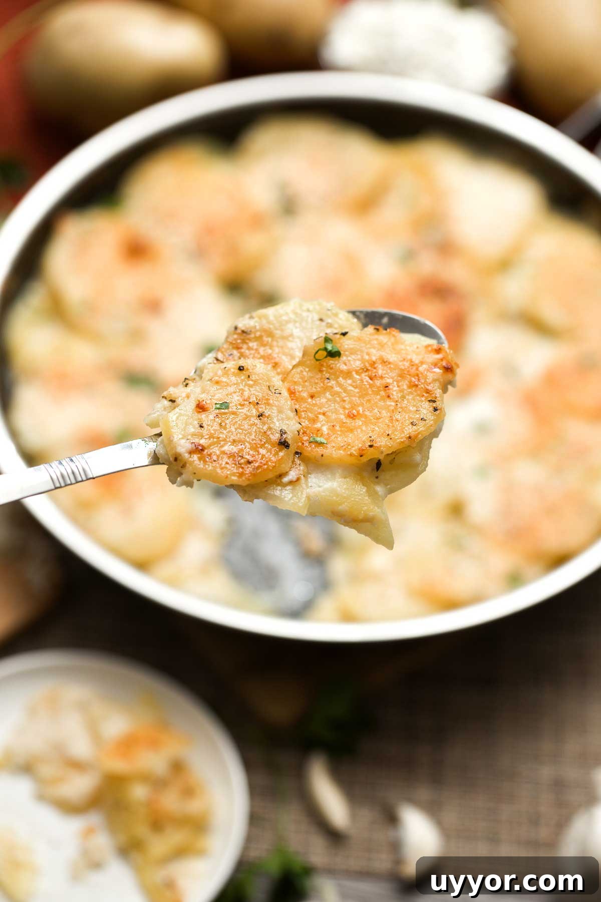 A close-up of a large spoon with cheesy au gratin potatoes over a Hexclad skillet.