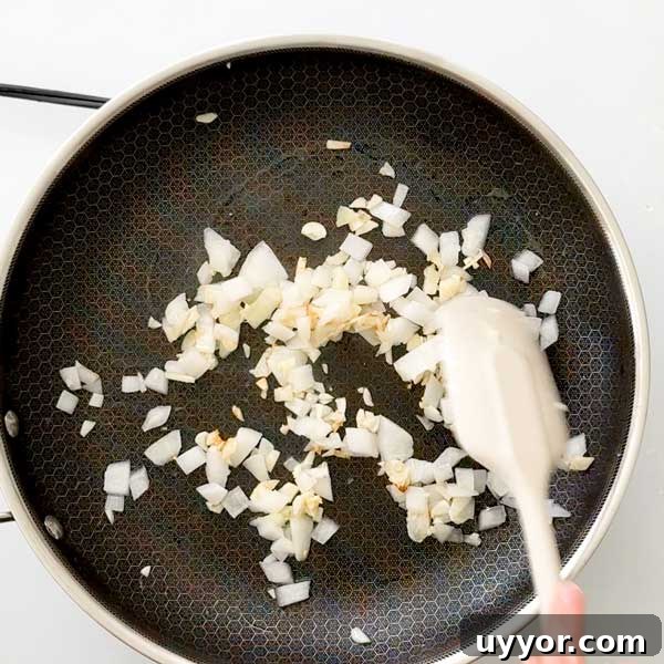 Diced onions and garlic sautéed in a skillet with a spatula.