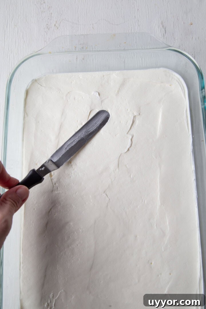 Strawberry Pretzel Salad Recipe with Creamy Cheesecake Layer 8 spatula spreading a white filling into a baking dish.
