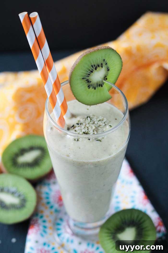 Mango Kiwi Smoothie with Hemp Hearts - A tropical twist on a creamy smoothie. Sweetened only with fruit. Loaded with vitamin C, a good amount of protein and healthy fats. A vibrant green kiwi slice garnishes a tall glass of kiwi mango hemp smoothie with 2 orange and white paper straws.