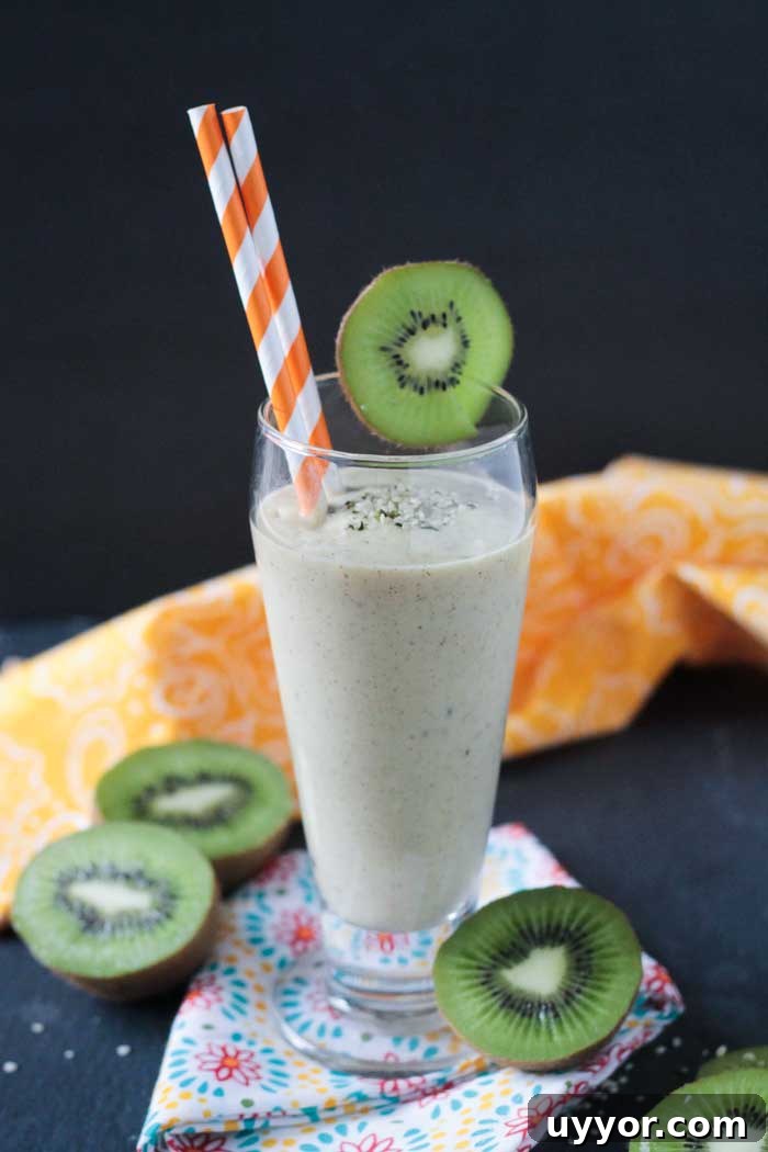 Mango Kiwi Smoothie with Hemp Hearts - A tropical twist on a creamy smoothie. Sweetened only with fruit. Loaded with vitamin C, a good amount of protein and healthy fats. Mango Kiwi Smoothie with Hemp Hearts in a tall glass, kiwi slice on side of glass as a garnish, 2 orange and white striped straws in the glass. Fresh kiwi slices surrounding the glass on the table.