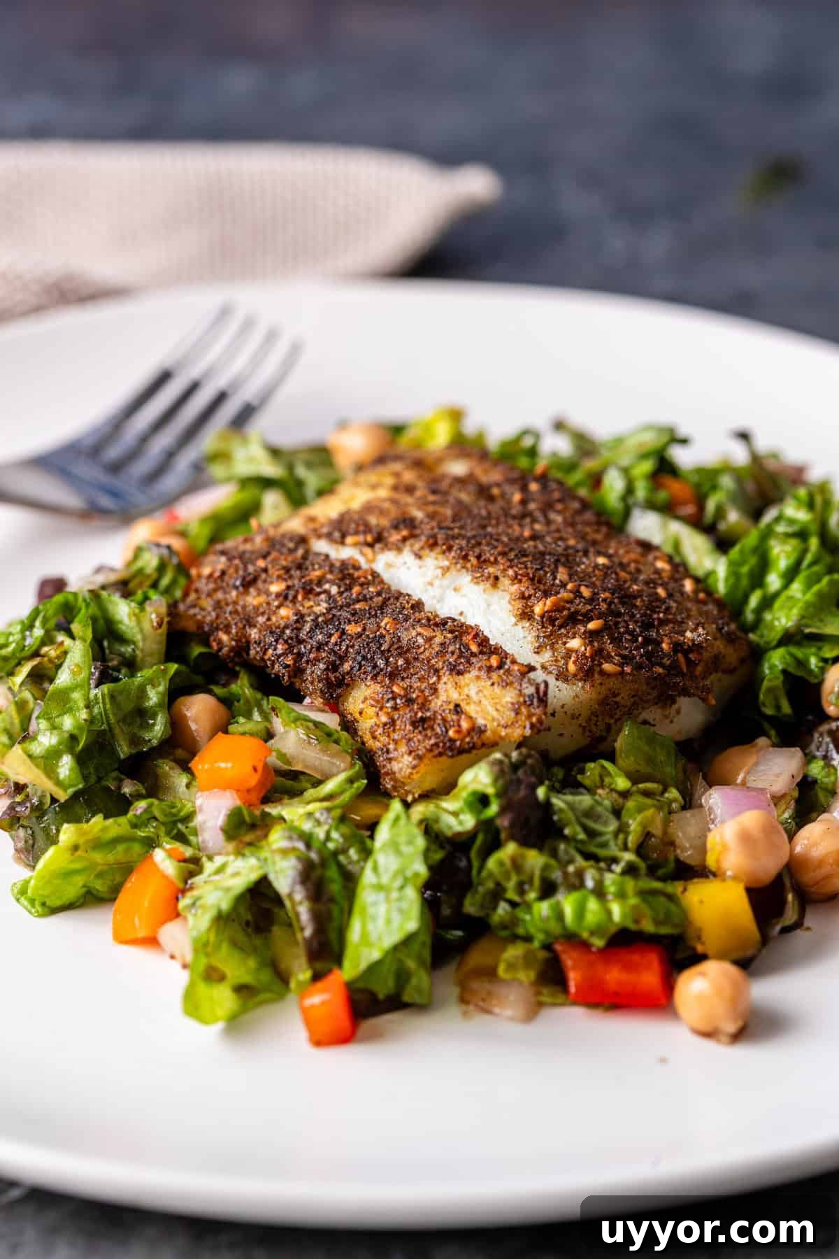 pan fried cod over a fresh salad on a white plate