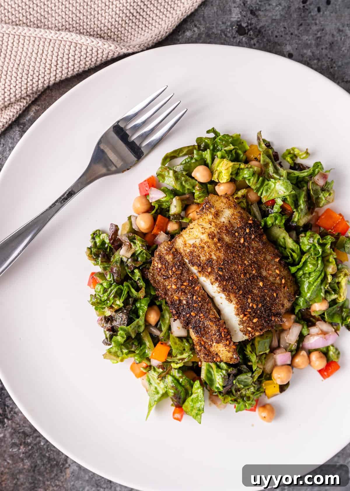 overhead: my cod recipe after pan frying over a salad on a white plate with a fork