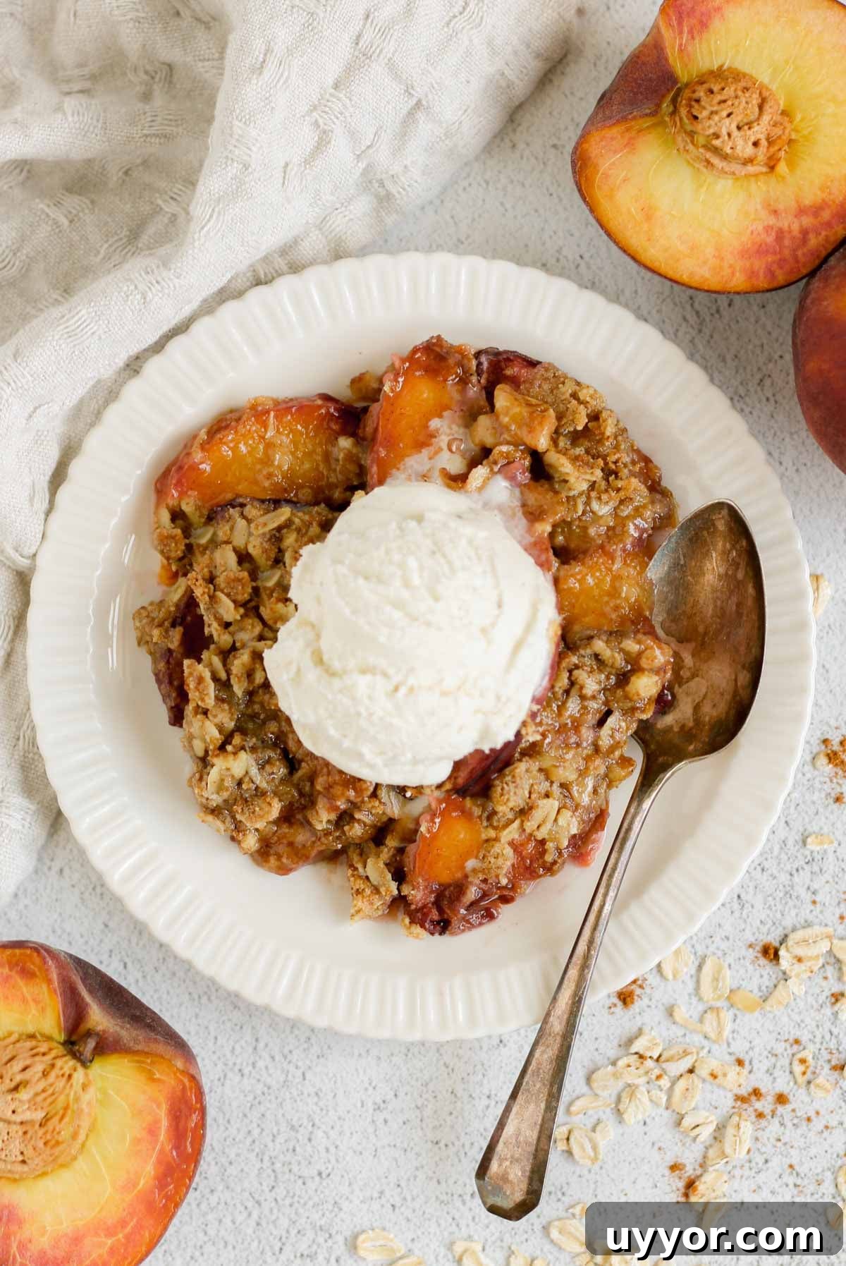 Whole-Grain Peach Crisp with Low Sugar Recipe 2 Serving of peach crisp on a round plate topped with ice cream and a vintage spoon on the plate with sliced peaches on the sides of the plate.