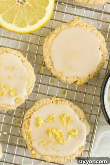 Almond flour lemon cookies topped with a glaze on a rectangular wire cooling rack with slices of lemon placed on the rack.