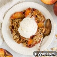 Whole-Grain Peach Crisp with Low Sugar Recipe 16 Serving of peach crisp on a round plate topped with ice cream and a vintage spoon on the plate with sliced peaches on the sides of the plate.