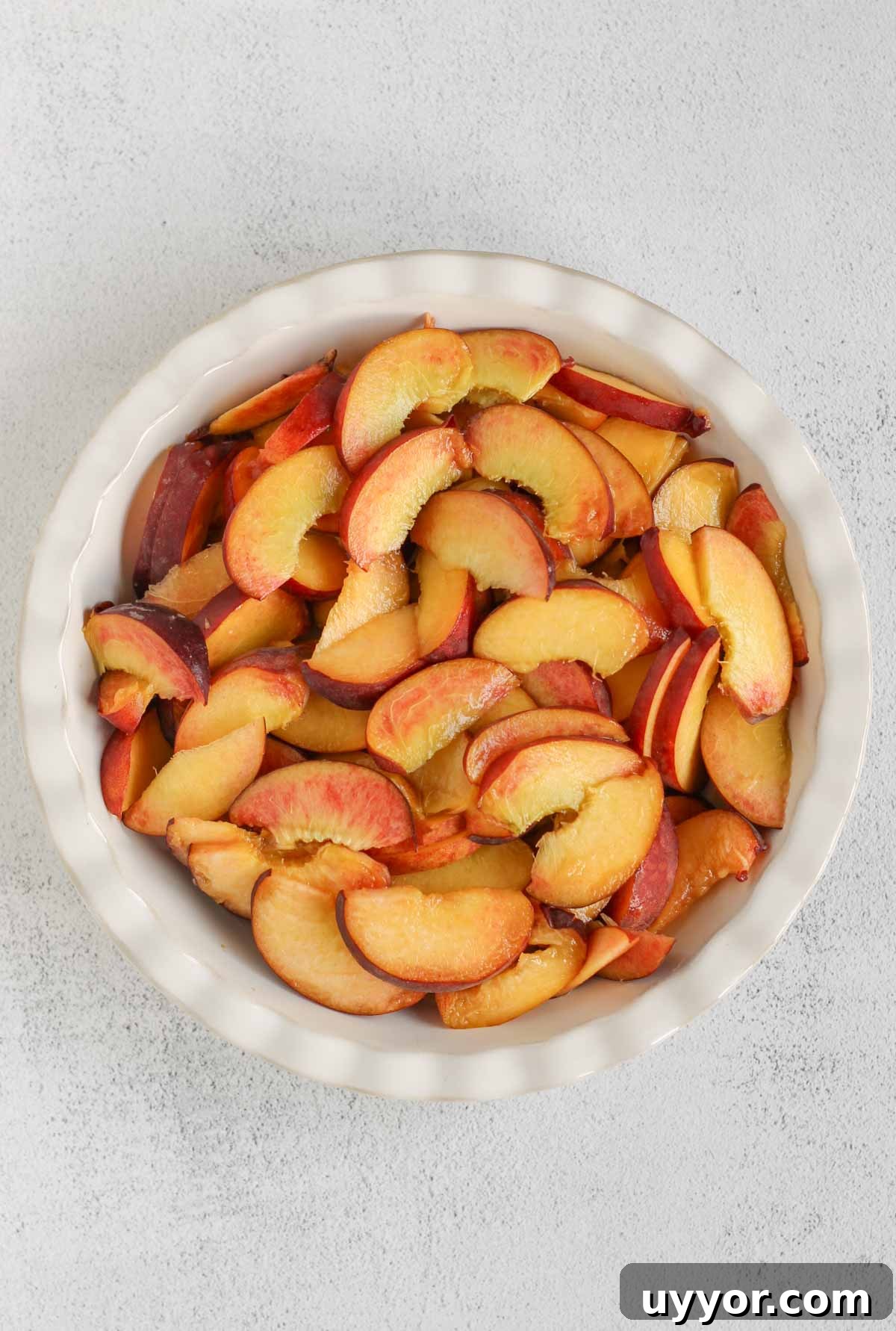 Whole-Grain Peach Crisp with Low Sugar Recipe 4 Sliced peaches in a ceramic pie plate.