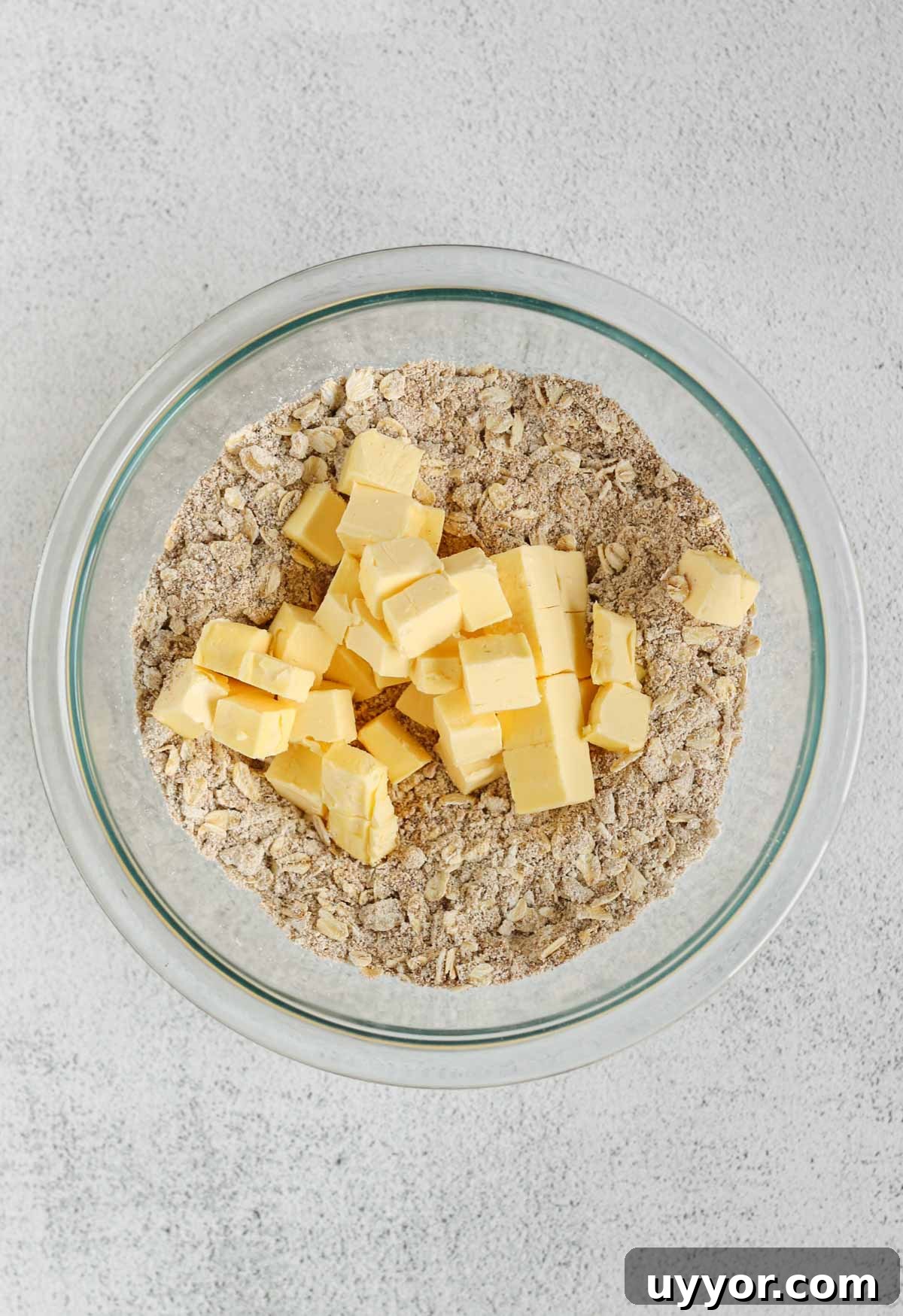 Whole-Grain Peach Crisp with Low Sugar Recipe 6 Oats, oat flour, and coconut sugar mixed in a small glass mixing bowl with cubes of butter added to the bowl.