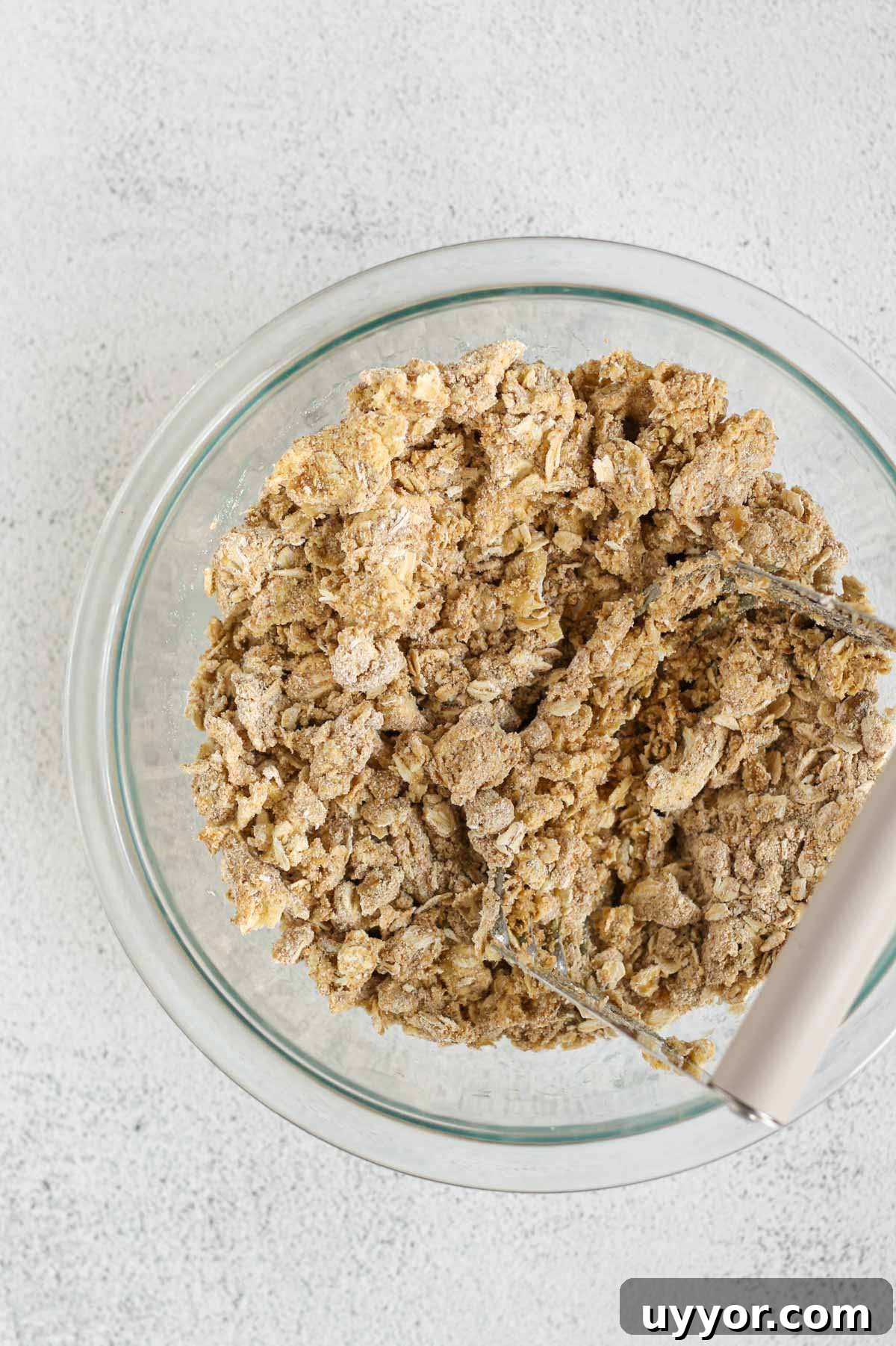 Whole-Grain Peach Crisp with Low Sugar Recipe 7 Pastry cutter cutting butter into a mixture of oats, oat flour and coconut sugar in a small glass mixing bowl.