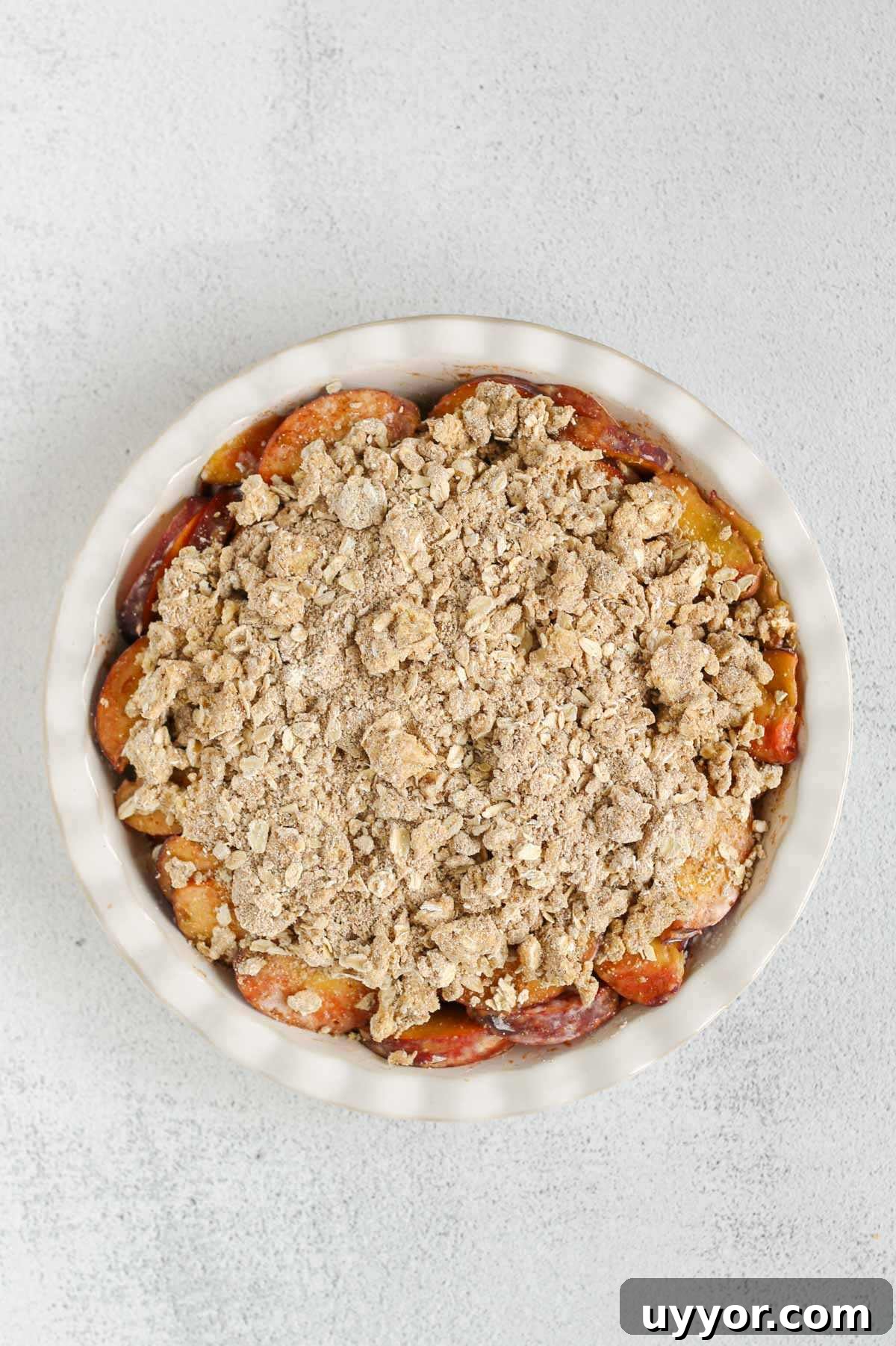 Whole-Grain Peach Crisp with Low Sugar Recipe 8 Sliced peaches in a ceramic pie dish topped with oat flour, oat, and butter mixture.