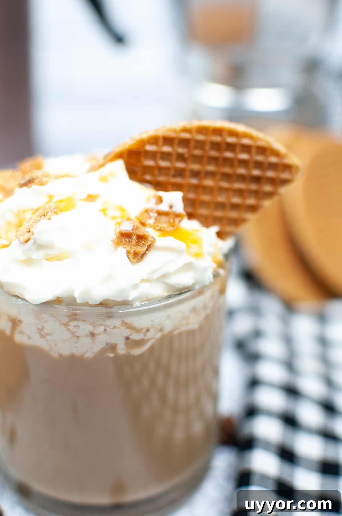 Copycat Crème Brûlée Latte Recipe Like Starbucks 4 A garnished latte in a glass sits on a white surface next to a checkered tea cloth.
