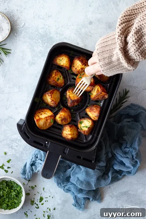 Air Fryer Cooking Times UK: Quick Guide by Food Type 4 Someone forking an air fryer roast potato in an air fryer drawer