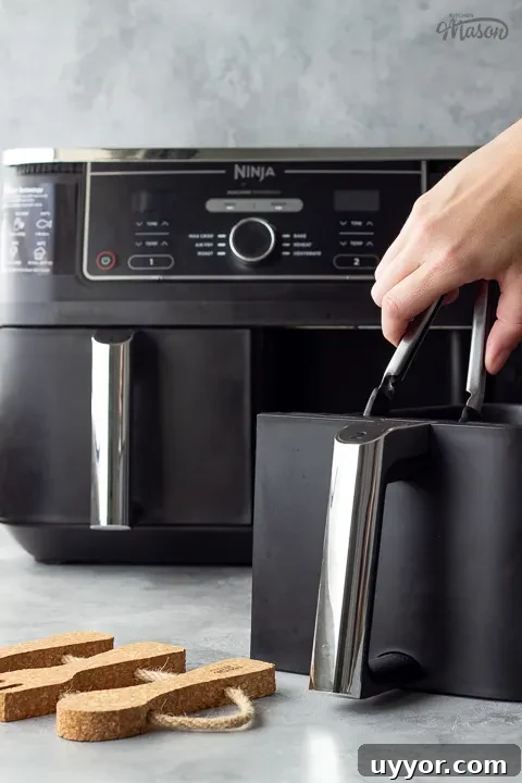 Air Fryer Cooking Times UK: Quick Guide by Food Type 5 Someone getting food out of an air fryer drawer. A text overlay says 'Ninja Foodi Air Fryer Review'