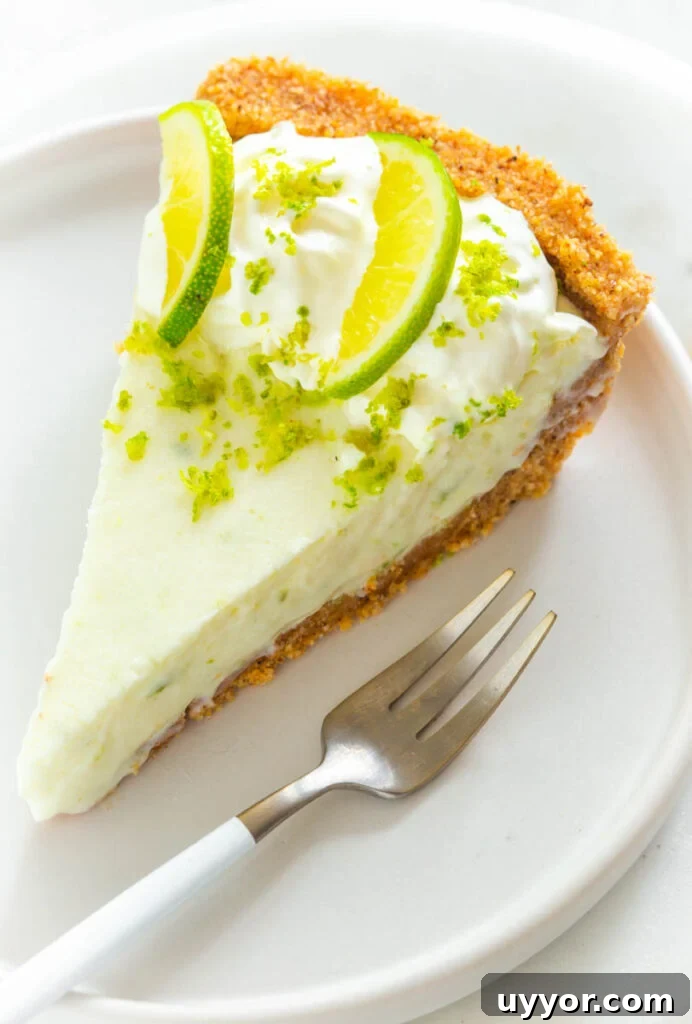 a slice of keto low carb key lime pie on a white plate with fresh limes and a fork