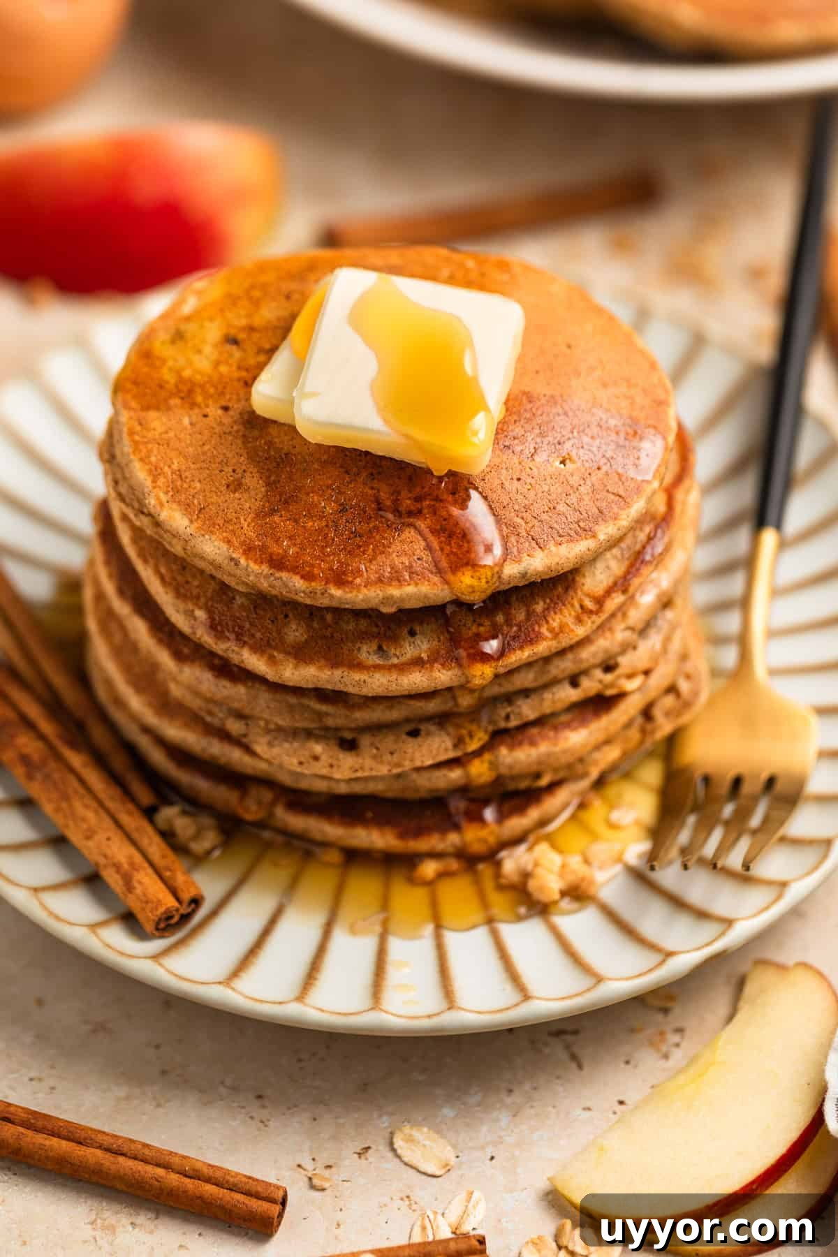 Stack of apple oatmeal pancakes on plate topped with butter and syrup.