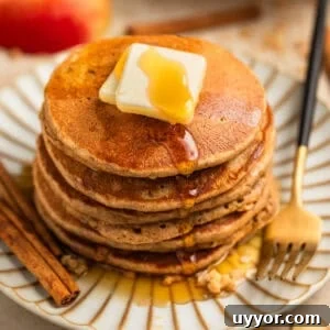 Stack of pancakes on plate with butter and maple syrup and cinnamon sticks beside.