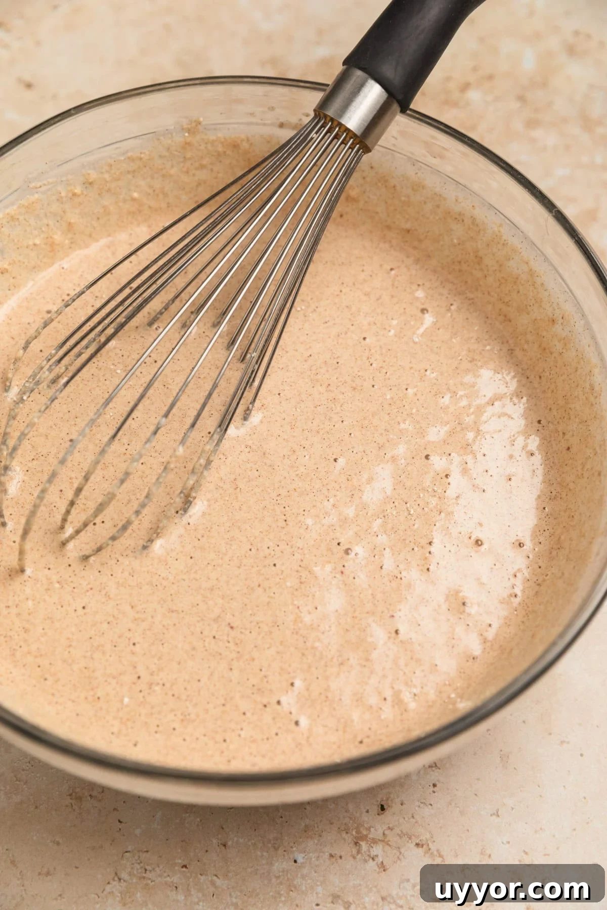 A bowl of apple oatmeal pancake batter with a whisk in it.