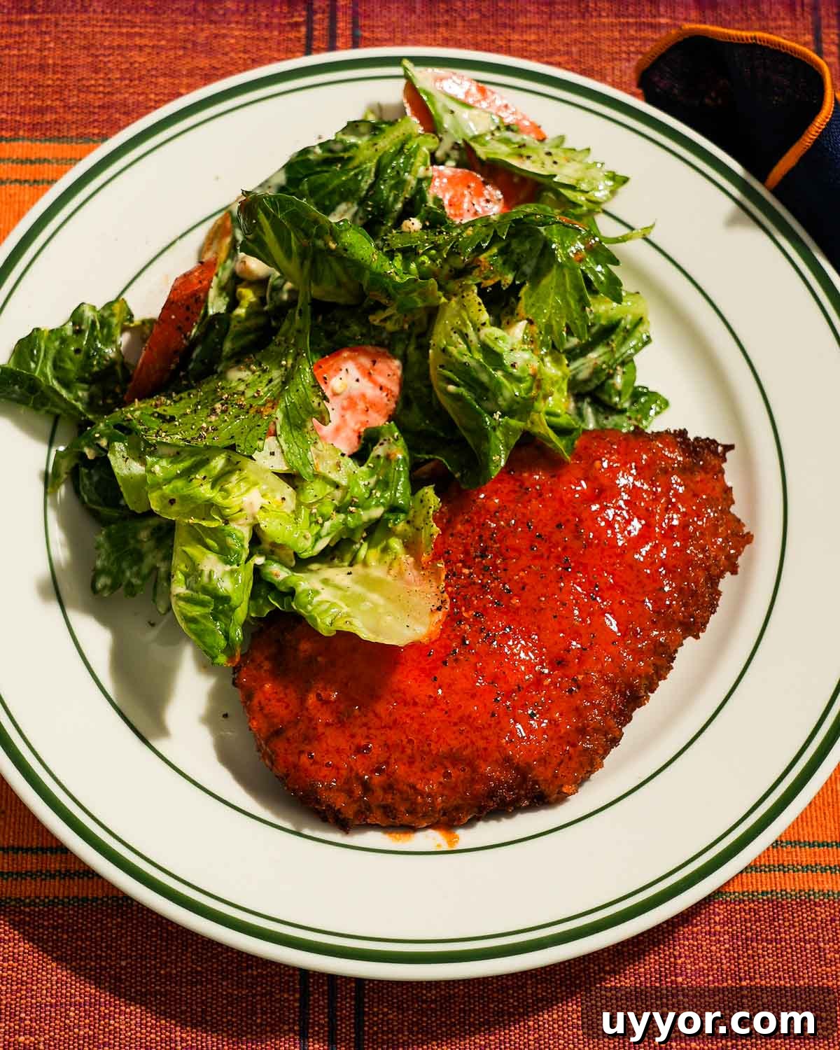 Crispy Panko Buffalo Chicken Cutlets With Tangy Sauce 2 Buffalo chicken cutlet alongside dressed salad with cracked pepper garnish.