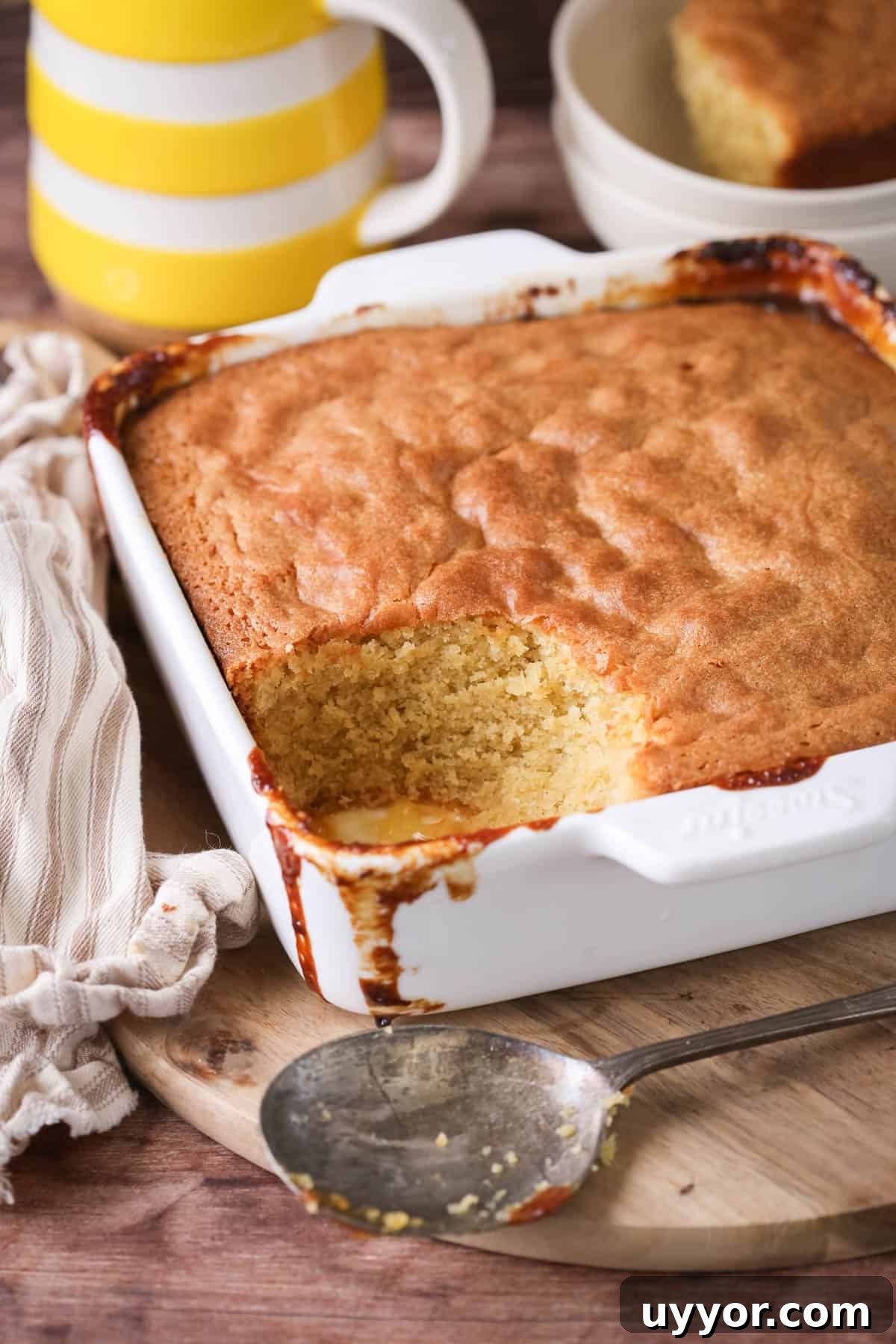 Gluten-Free Lemon Curd Sponge Pudding Recipe for Zesty Dessert 2 Lemon sponge pudding in a baking dish with a scoop taken out showing moist sponge.