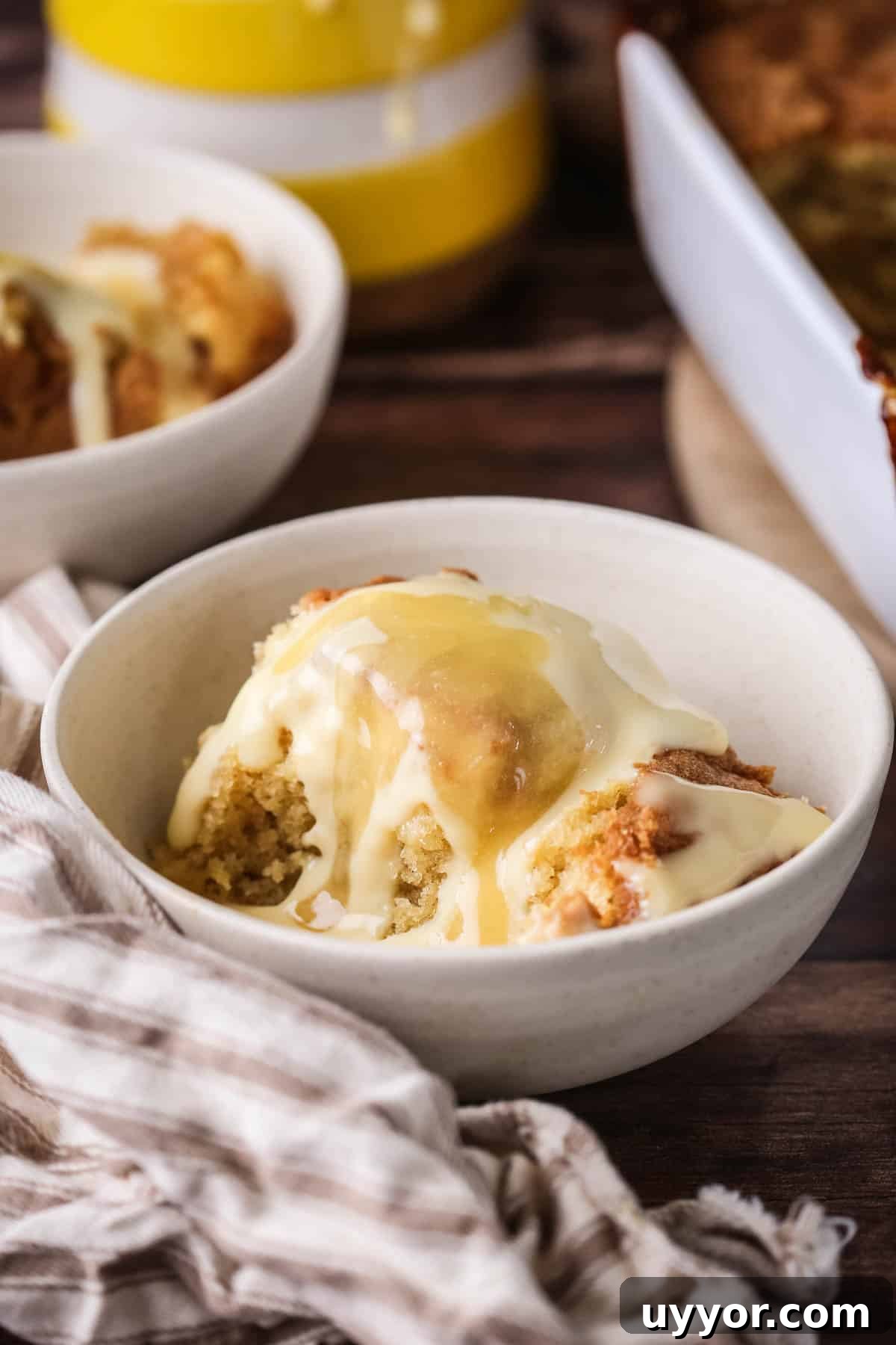 Gluten-Free Lemon Curd Sponge Pudding Recipe for Zesty Dessert 12 Portion of lemon pudding in a bowl with custard poured over top and extra lemon curd drizzled over.