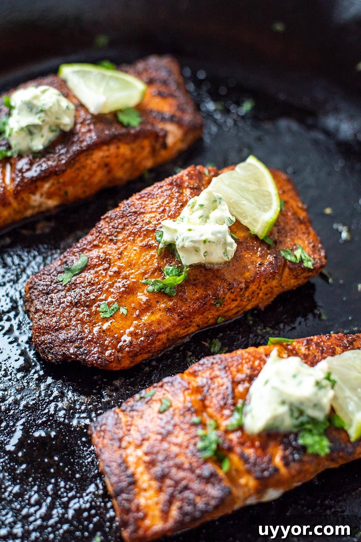 Golden blackened salmon filets in a cast iron skillet topped with herb butter and a lime wedge.