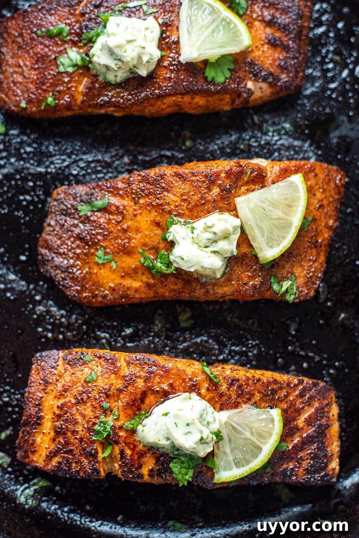Golden blackened salmon filets in a cast iron skillet topped with herb butter and a lime wedge.