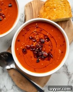 overhead shot of red pepper soup served in white bowl on wooden board with spoon and grilled cheese
