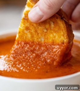 close up shot of hand dunking grilled cheese into small white bowl of soup