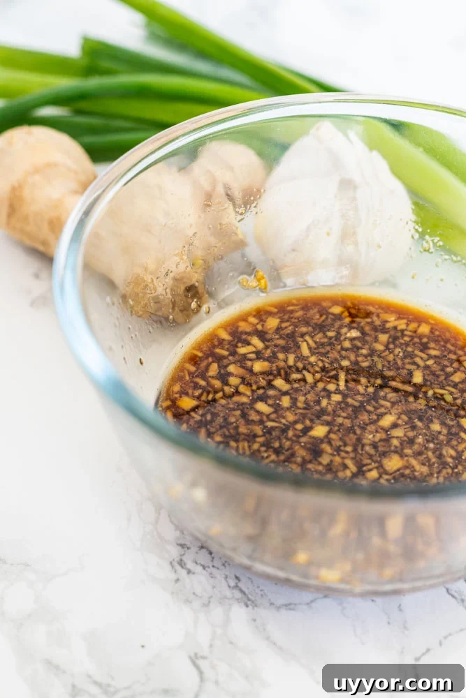 Sauce for Korean beed bowls in a bowl on a counter wth spring onions, garlic, and ginger.