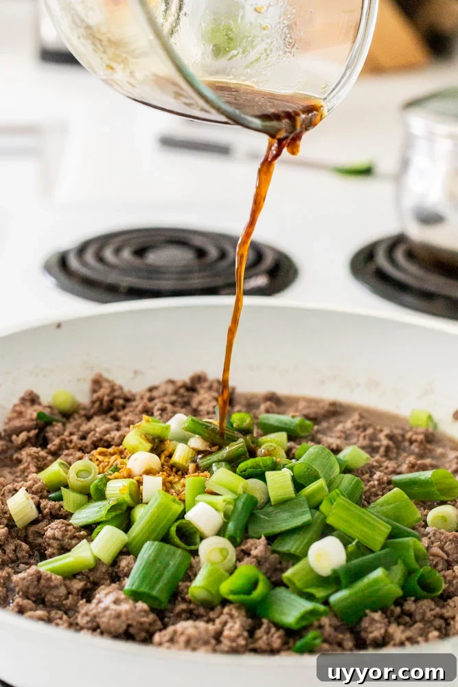 Pouring sauce into a skillet with browned beef and green onions.