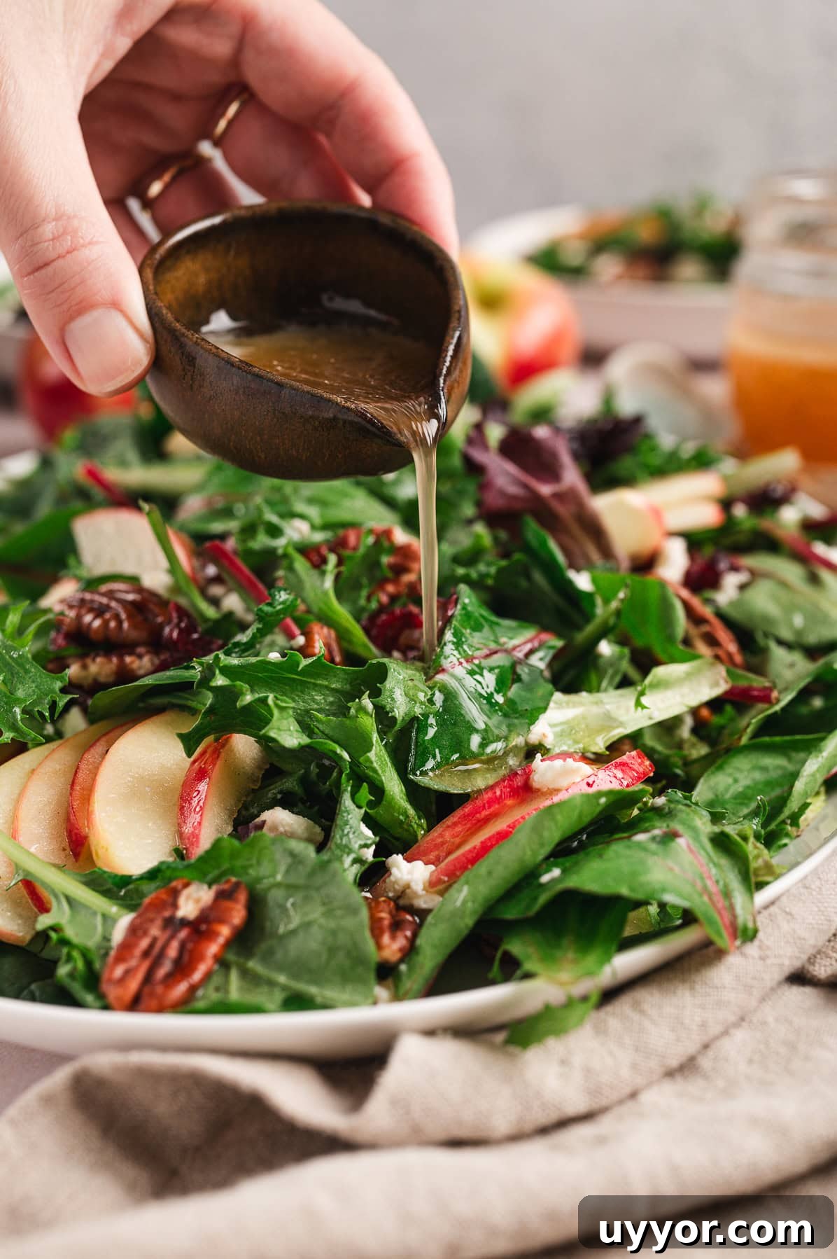 a vessel of dressing pouring onto a leafy apple salad