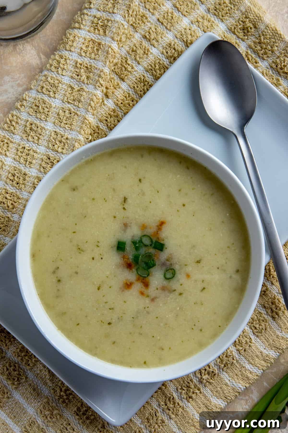 Creamy Keto Cauliflower Soup Recipe – Low-Carb Comfort Bowl 5 Overhead view of soup in round white bowl sitting on white square plate. Soup topped with sliced green onions.