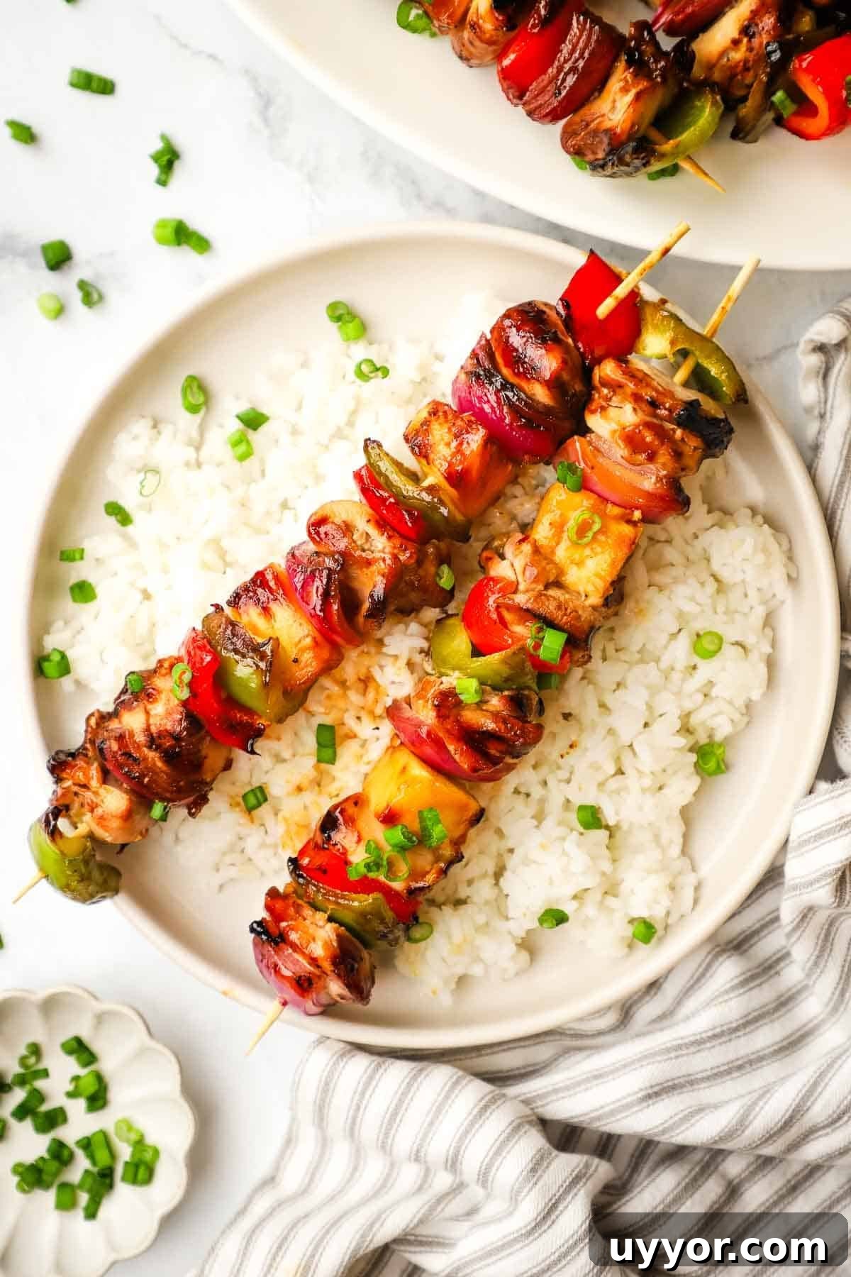 Sticky Teriyaki Chicken Skewers with Grilled Pineapple 2 A plate of teriyaki chicken and vegetable skewers served over rice.