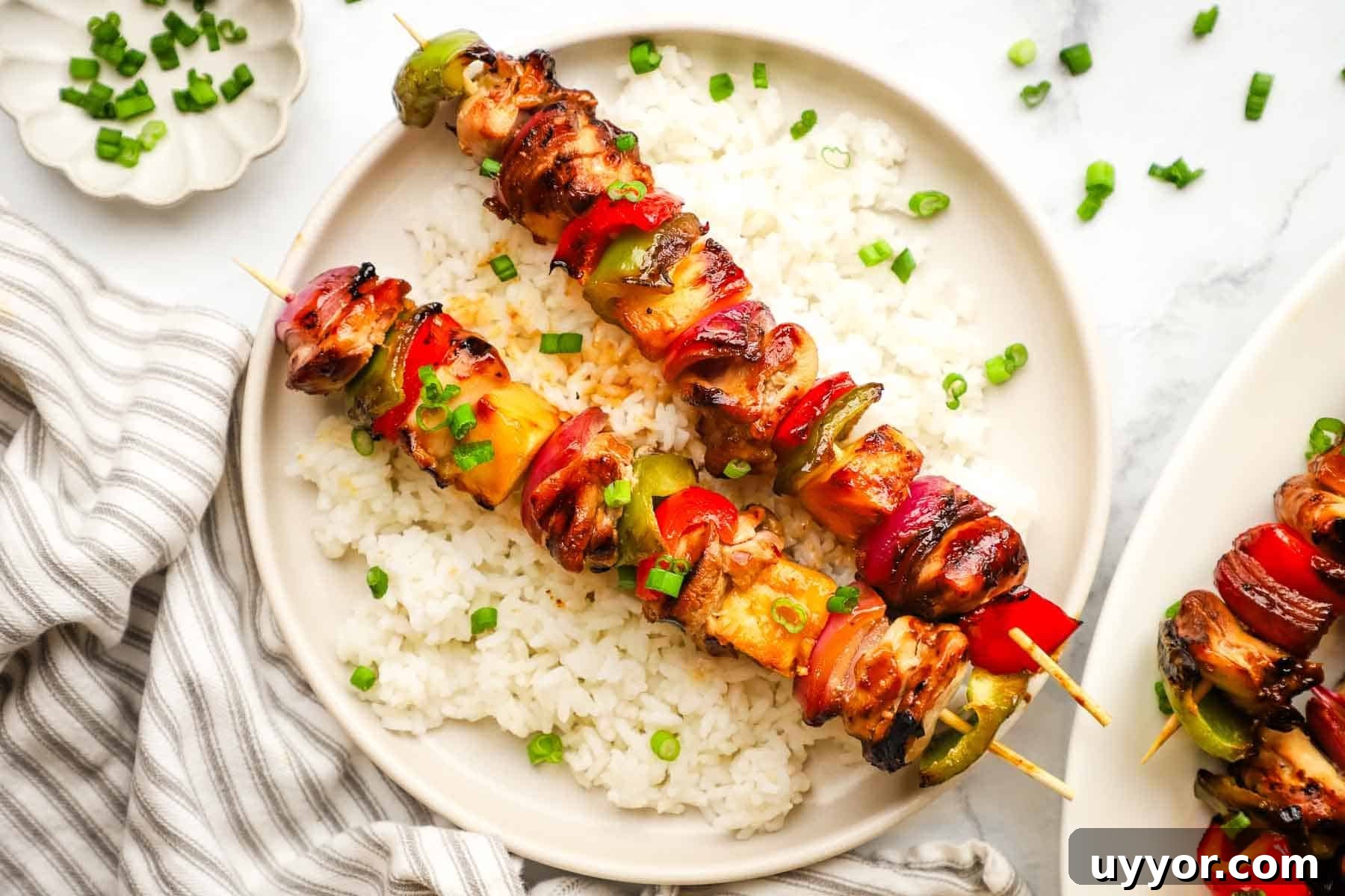 Sticky Teriyaki Chicken Skewers with Grilled Pineapple 8 A plate of teriyaki chicken and vegetable skewers served over rice.