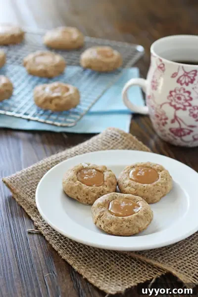 These dreamy caramel latte thumbprint cookies are perfectly soft, thick and filled with coffee flavor. With gooey caramel and finished with a touch of sea salt, they are perfect for holiday cookie trays! Caramel Thumbprint Cookies on a plate with coffee to the side.