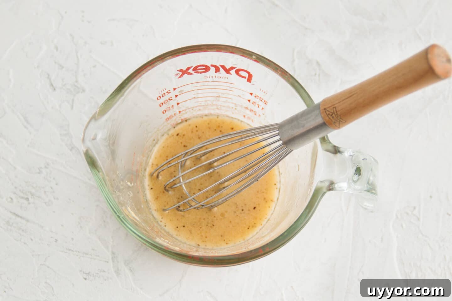 Picture of measuring cup with vinaigrette and whisk.