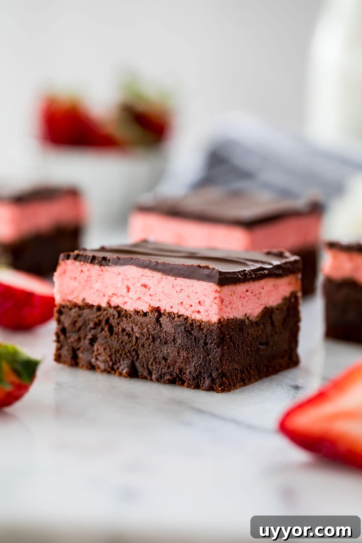 close-up view of a strawberry brownie consisting of a brownie layer, strawberry icing layer, and a final layer of chocolate ganache
