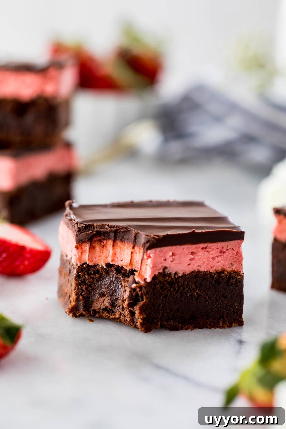 thick, square-cut brownie layered with pink strawberry frosting and chocolate ganache with a bite missing from one corner