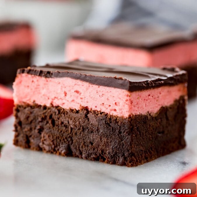 close-up view of a strawberry brownie consisting of a brownie layer, strawberry icing layer, and a final layer of chocolate ganache