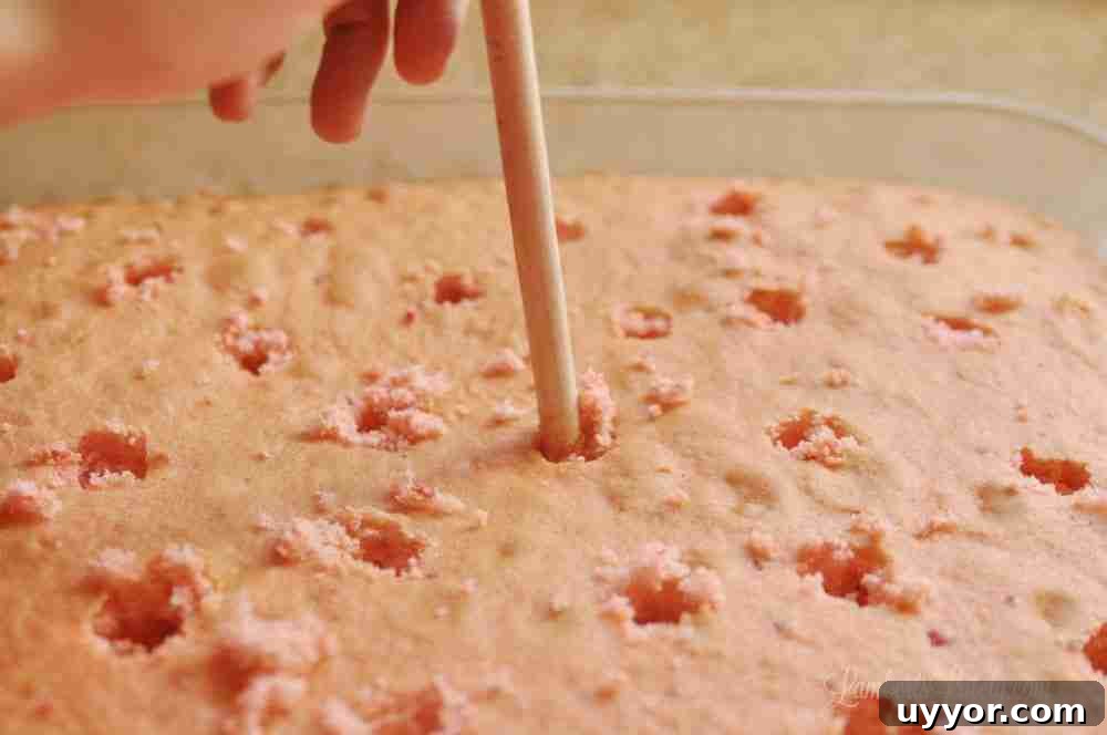 Strawberry Banana Pudding Cake Recipe — Moist Layer Cake 4 punching holes in a cake with the back of a wooden spoon.
