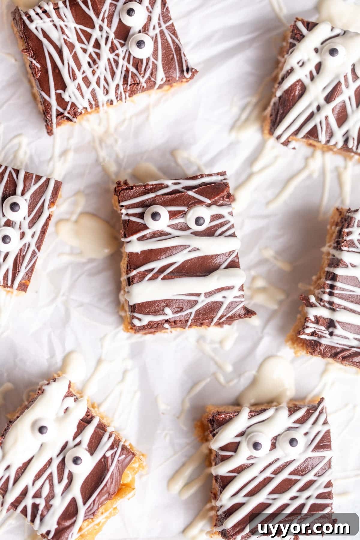 Halloween Scotcheroos Recipe: Spooky No-Bake Peanut Bars 2 Halloween Scotcharoos drizzled with white chocolate and decorated with edible eyes on a piece of parchment paper.