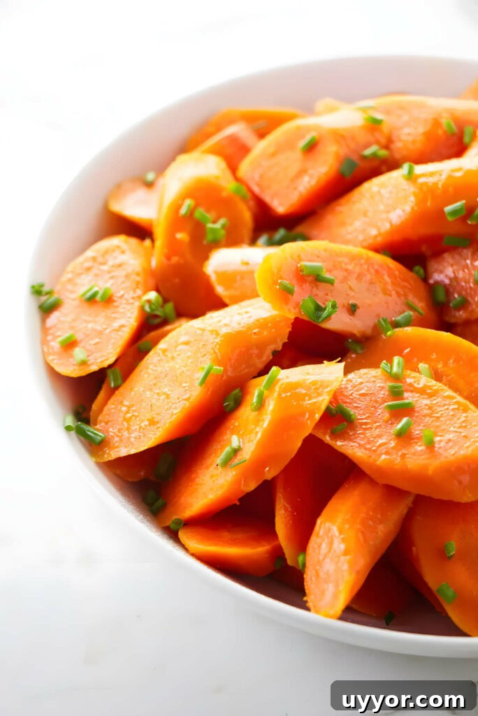 A serving bowl filled with steamed carrots garnished with chives.