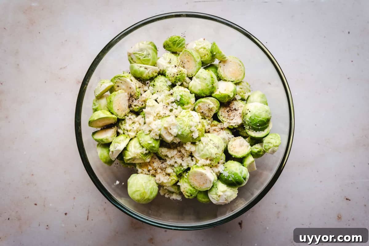 halved brussels sprouts tossed with oil seasoning and garlic in a glass bowl.
